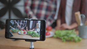 online blogging, mobile phone makes video for subscribers how bloggers couple cook preparing healthy meals from fresh vegetables and greens close up on kitchen table