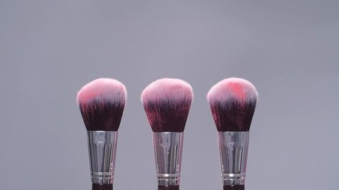 Make-up brush with pink powder splashes explosion on gray background on slow motion