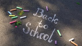 Closeup top view of phrase Back to school drawn with white chalk on grey surface of sidewalk. Zooming. Real time 4k video footage.