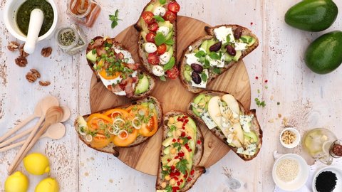 Assorted  open faced sandwiches, Open avocado sandwiches made of  slices of sourdough bread with  various toppings on a round board, on a white wooden table, top view, 4k.