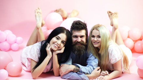 Cheerful morning concept. Man and women, friends on smiling faces lay, pink background. Lovers in love happy together. Bearded man and women in domestic clothes, pajamas. Threesome relaxing in morning