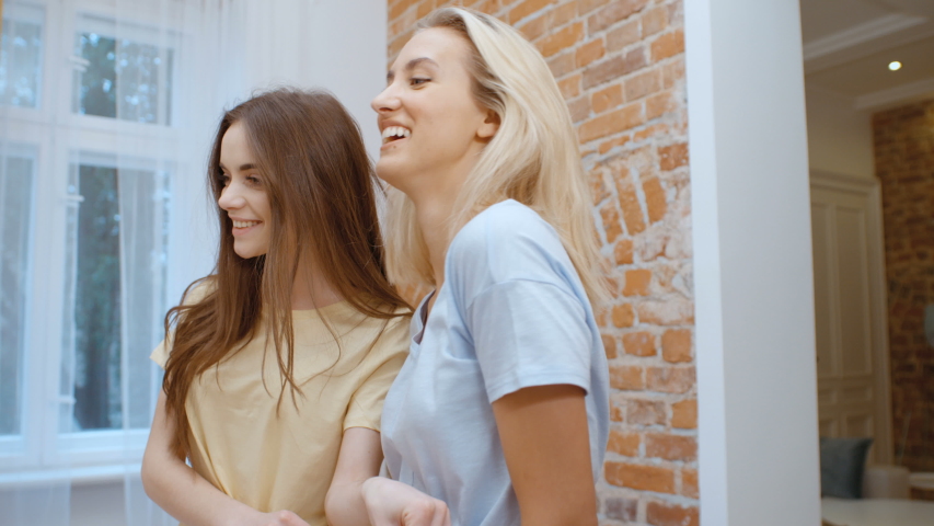 Two cheerful young girlfriends trying on clothes at home. Royalty-Free Stock Footage #1031559323