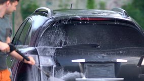 Young man spraying down his car with soapy water