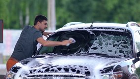 Young man washing his windscreen with soap