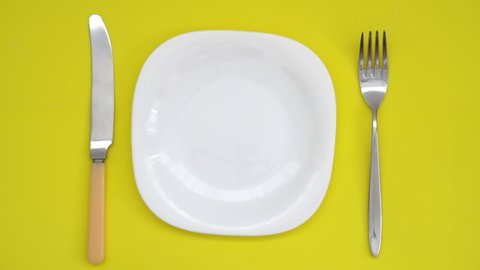 Healthy eating concept. top view of a white plate with a fork and knife on a yellow background on which the male hand puts a sweet cake drenched in chocolate.