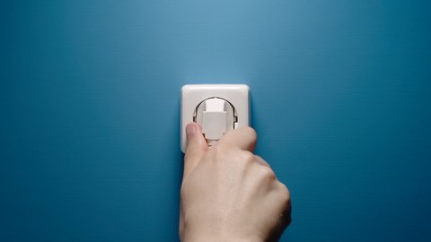 Man Inserts Plug Into Electrical Socket On A Blue Wall