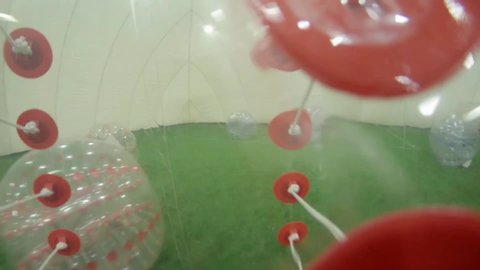 Dynamic camera demonstrates from inside of soccer inflatable bubble wrap of running man on green plastic grass in small isolated football field covered by white dome.