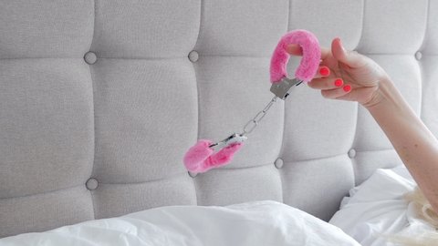 Pink sexy fluffy handcuff hanging on female finger, closeup. Erotic sex game with sexual bdsm toy in bedroom interior, no face