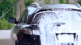 Young man hosing down a soapy car with a high pressure nozzle during cleaning
