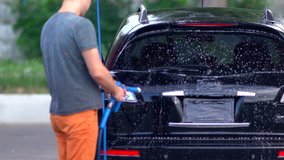 Young man spraying foam on his car at a car wash as he prepares to clean the bodywork and tyres using a high pressure hose