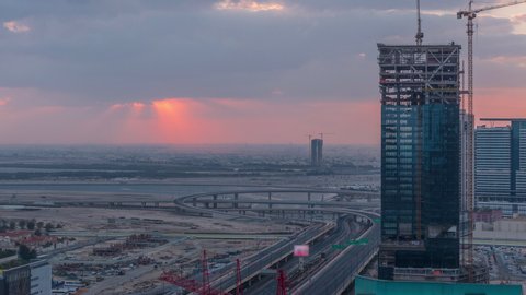 Sunrise aerial view of Financial center road morning timelapse with intersection and under construction building with cranes from downtown, Dubai Creek harbor on background