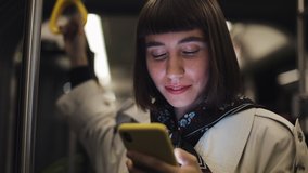 Portrait of young hipster woman holds the handrail, using smartphone standing in public transport. City lights background. - Powered by Shutterstock - Get 15% off with code: PIKWIZARD15
