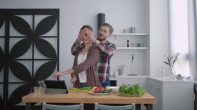 portrait of smiling loving couple in cuisine, happy girl with guy prepares healthy food for dinner with fresh vegetables on kitchen table using tablet with video recipe
