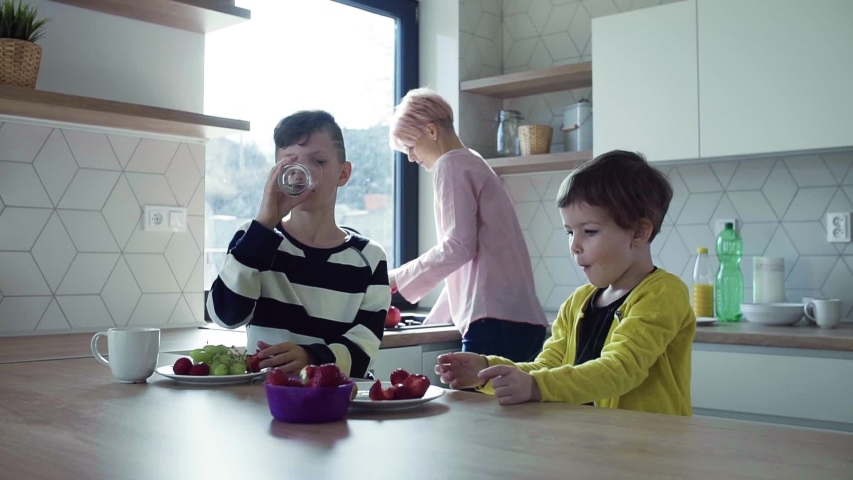 A young mother with two children eating fruit in a kitchen. | Shutterstock HD Video #1031600981