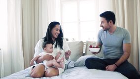 Young happy couple with a baby indoors on bed, eating strawberries. - Powered by Shutterstock - Get 15% off with code: PIKWIZARD15
