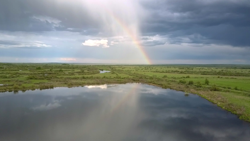 wonderful rainbow and blue thick clouds reflected in calm lake water in summer bird eye flight. Concept countryside and environmental change
