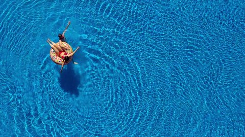 Aerial view of couple having fun in the pool, man is swimming and a woman is lying on an inflatable donut