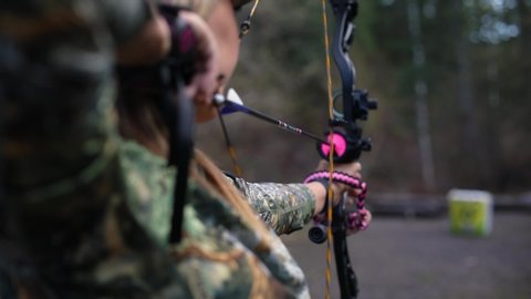A girl holding a bow and arrow which is pulled back and ready to fire at the target.