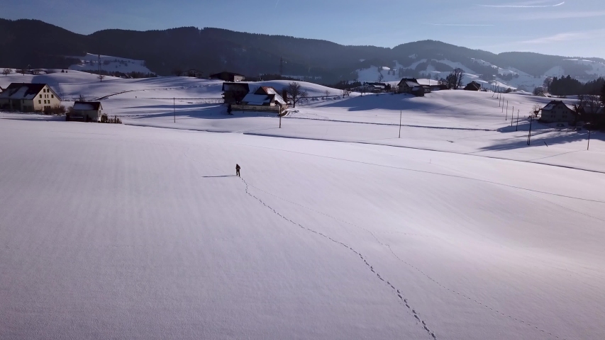 Young man walks in a huge snowy field and stops and looks around in Switzerland while winter.