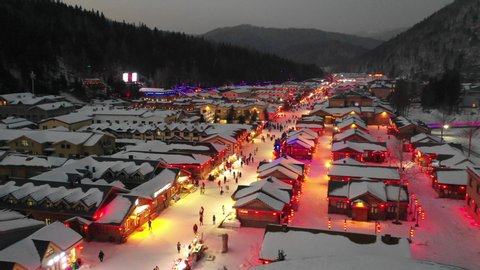 China Winter travel and nightlife - Drone flight of popular snow town, with pedestrians walking and sledding through its main street at night 스톡 비디오