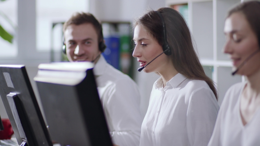 Polite young and beautiful call center operator answers the call with headset and types the information via keyboard of the computer. Professional service, psychological support, career. Modern office | Shutterstock HD Video #1031614160