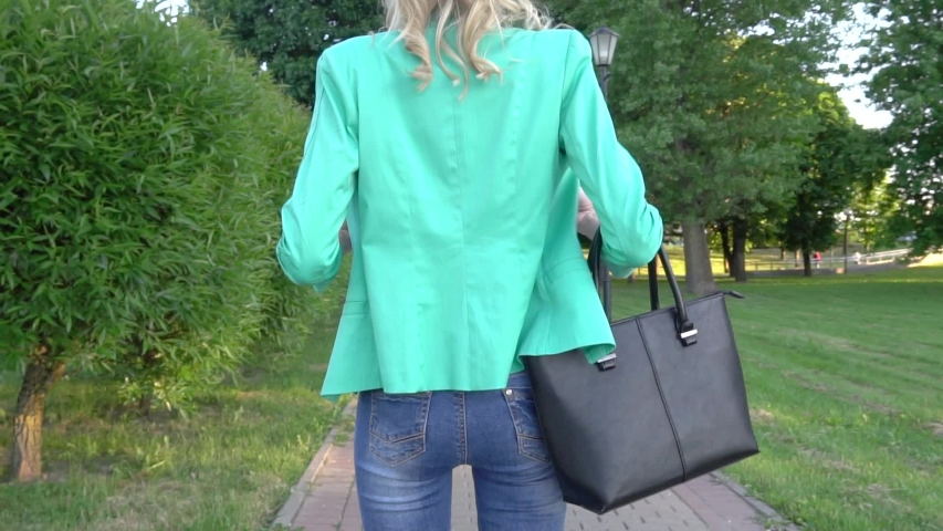 Rear view, the girl is spinning. young slender Caucasian blonde walking along the alley of decorative and neat tall green trees. On a sunny summer day. Slow motion girl spinning.