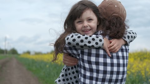 Happy child hugging mother. A little girl runs on a field of flowering canola to mom and hugs her.