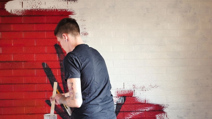 Person whitewashing a red painted brick wall
