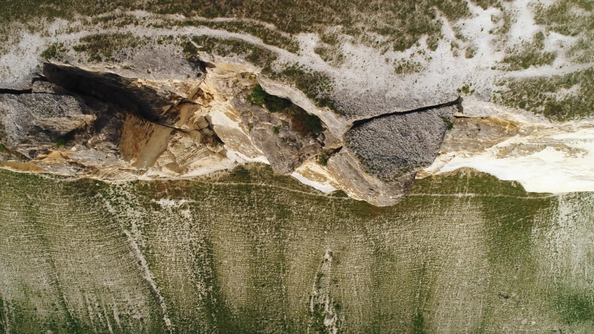 Aerial view of high cliff slope with white stones and bottom of the cliff covered with green grass. Shot. Contrast mountains landscape