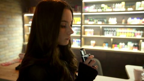 Vaping teenager. Young pretty white girl smoking an electronic cigarette in vape bar with problem skin. Bad habit.