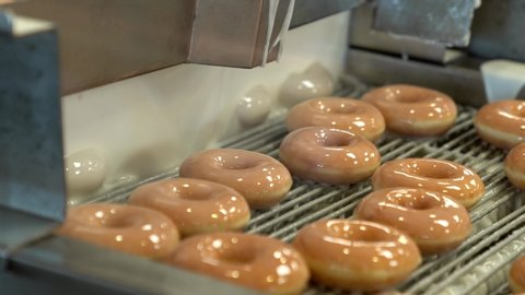 This video shows a busy donut factory glazing hot, fresh donuts on a production conveyor belt.