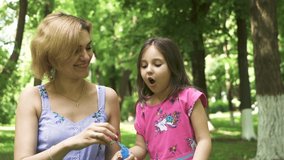  Attractive mother and daughter child blowing soap bubbles in summer city park