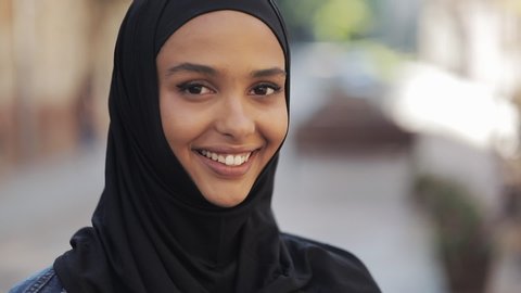 Portrait of beautiful young Muslim woman wearing hijab headscarf smiling into the camera standing on the old city background.