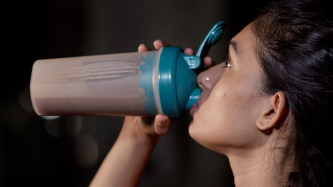 An attractive Indian girl drinking a protein shake after a workout in the gym