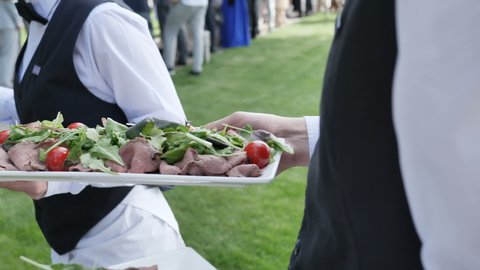 Catering service four waiters in their hands hold dishes from meat salami sausage tomatoes slow motion