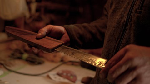 SLOW MOTION, CLOSE UP, DOF: Experienced bladesmith inserts a finished traditional knife into wooden sheath. Unrecognizable craftsman looks at the sharp ancient blade and puts it back into its case.