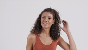 Caucasian girl plays with her curly, long, brown hair, enjoying herself while posing during a video and photo shoot.