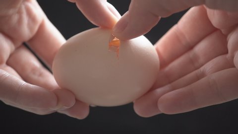 Female hands holding a cracked egg.Breaking an egg.Black background.Slow motion.