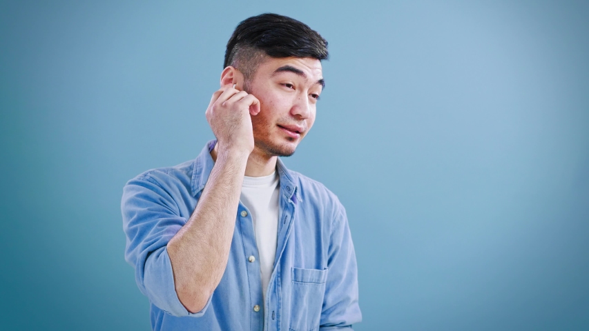 Young positive Asian guy speaking with friends on wireless headphones. 