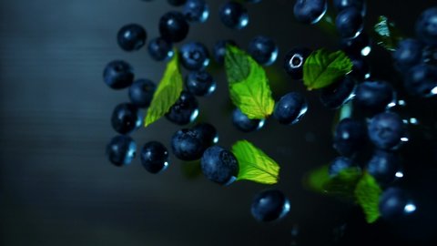Berries blueberries and mint leaves hang in the air on a dark background in slow motion. Macro shoting