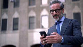 Cheerful mature male entrepreneur in optical eyeglasses enjoying video conversation with friend during break in downtown connected to public internet, happy man in formal suit communicating via app