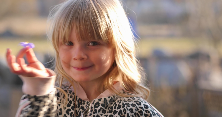 Handheld, slow motion shot of a little blonde girl smiling and showing a flower, found in the finnish countryside, on a sunny spring day, in Vaasa, Ostrobothnia, Finland