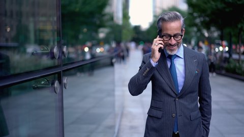Confident male successful lawyer calling via cellphone while strolling to meeting with clients, mature man in spectacles using roaming connection for making international call

