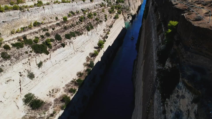 Amazing drone view of the Corinth Canal with a couple looking at a sail boat passing by.