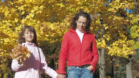 Mother with daughter walking around autumn forest. Yellow leaf boquet in childres hand.