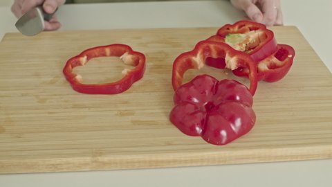 woman cuts red pepper with a knife on the kitchen board.