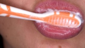 This macro video shows a person brushing their teeth with a bright orange toothbrush, very close up.
