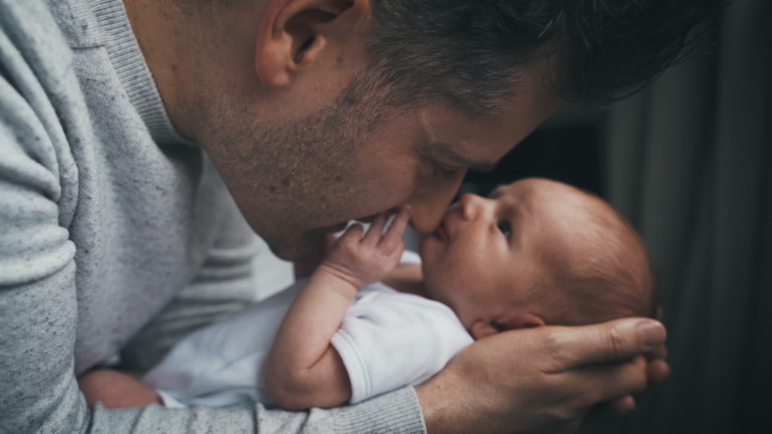 Newborn baby touches dad's face as they snuggle close together. Daddy and infant spend time face to face with loving looks and touches. Man holding tiny baby. Royalty-Free Stock Footage #1031713949