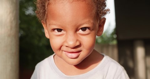 A close up shot of a young mixed raced child's face as he smirks and smiles into the camera.