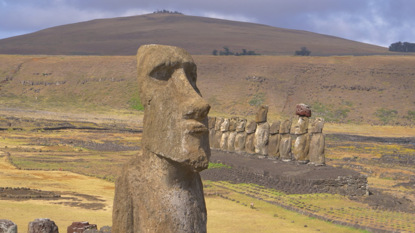 AERIAL, COPY SPACE: Flying around a mysterious monolithic structure with a human face. Spectacular shot of a large ancient sculpture towering above a group of smaller moais on famous Easter Island.